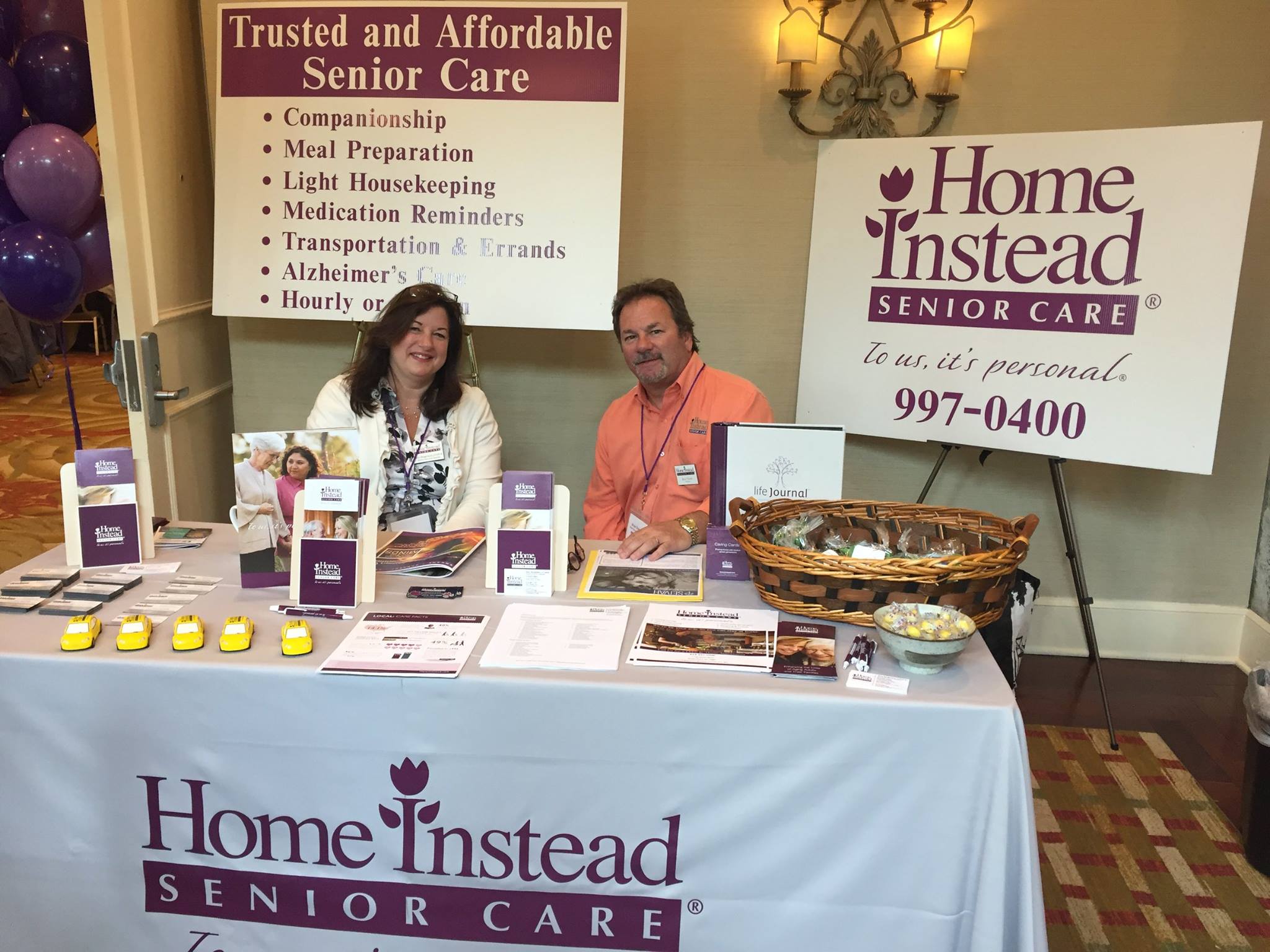 home instead owner and staff member sitting at senior fair booth