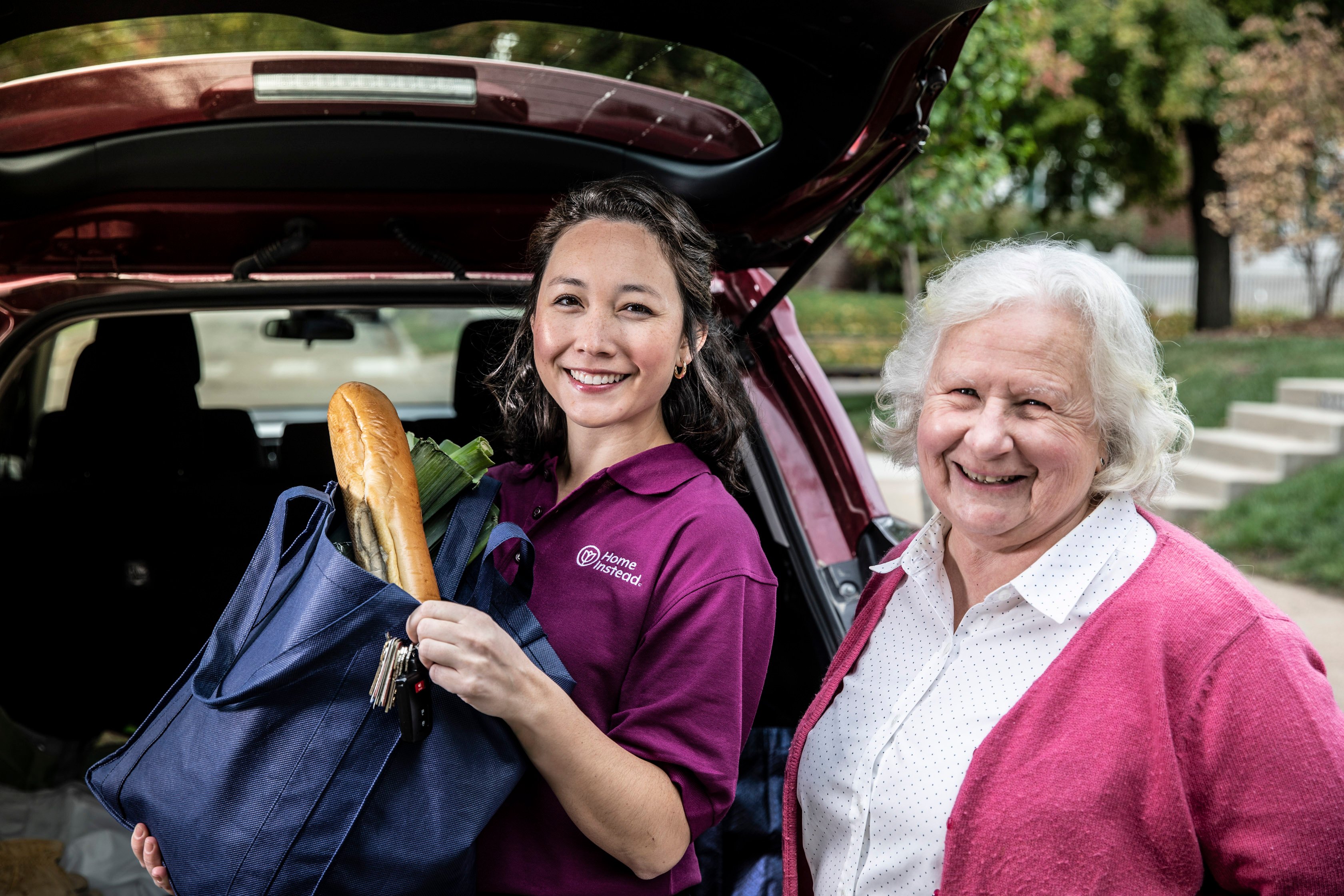 live-in caregiver getting groceries out of car for smiling female senior