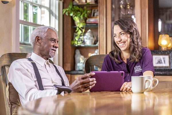 smiling caregiver sitting with senior using tablet