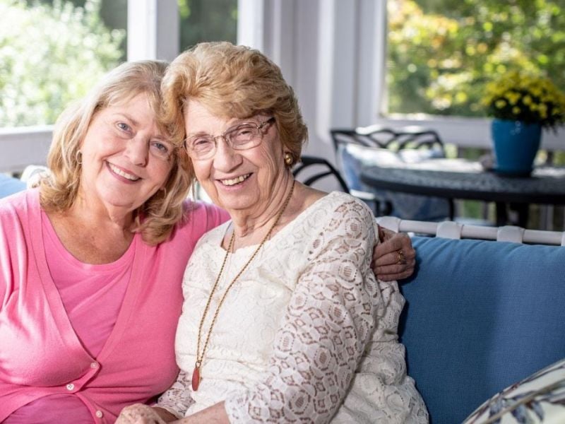 caregiver and client sitting on couch sharing a hug and warm smiles 