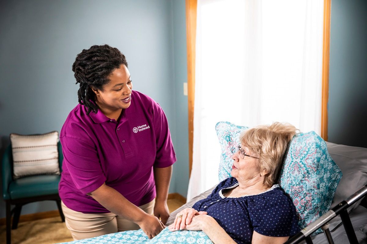 Home Instead Caregiver helping a senior in a hospital bed