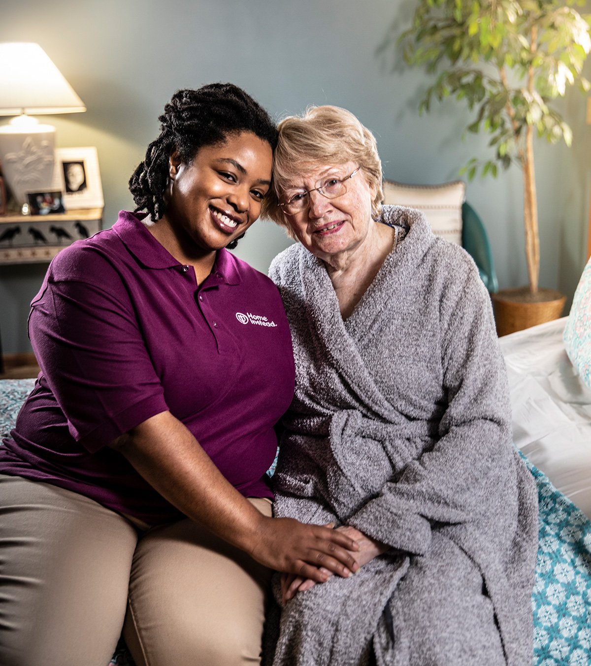 Home Instead Caregiver sitting on bed smiling with senior woman