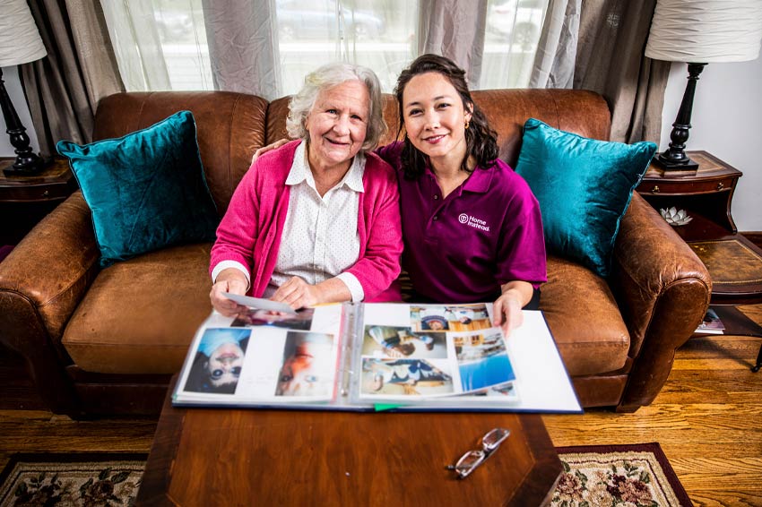 Senior woman and Home Instead caregiver enjoy photo album