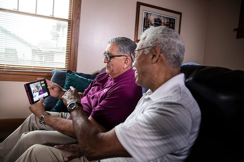 Home Instead CAREGiver and senior sitting on couch looking at tablet video call