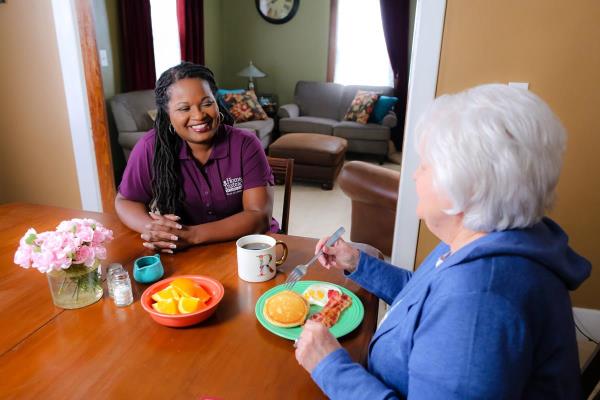 Home Instead Caregiver stands smiling in front of senior woman in bed