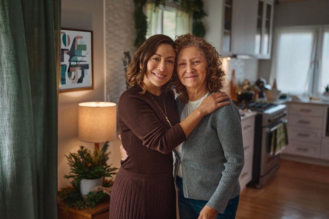 An adult daughter with her arm around her smiling mother in a kitchen