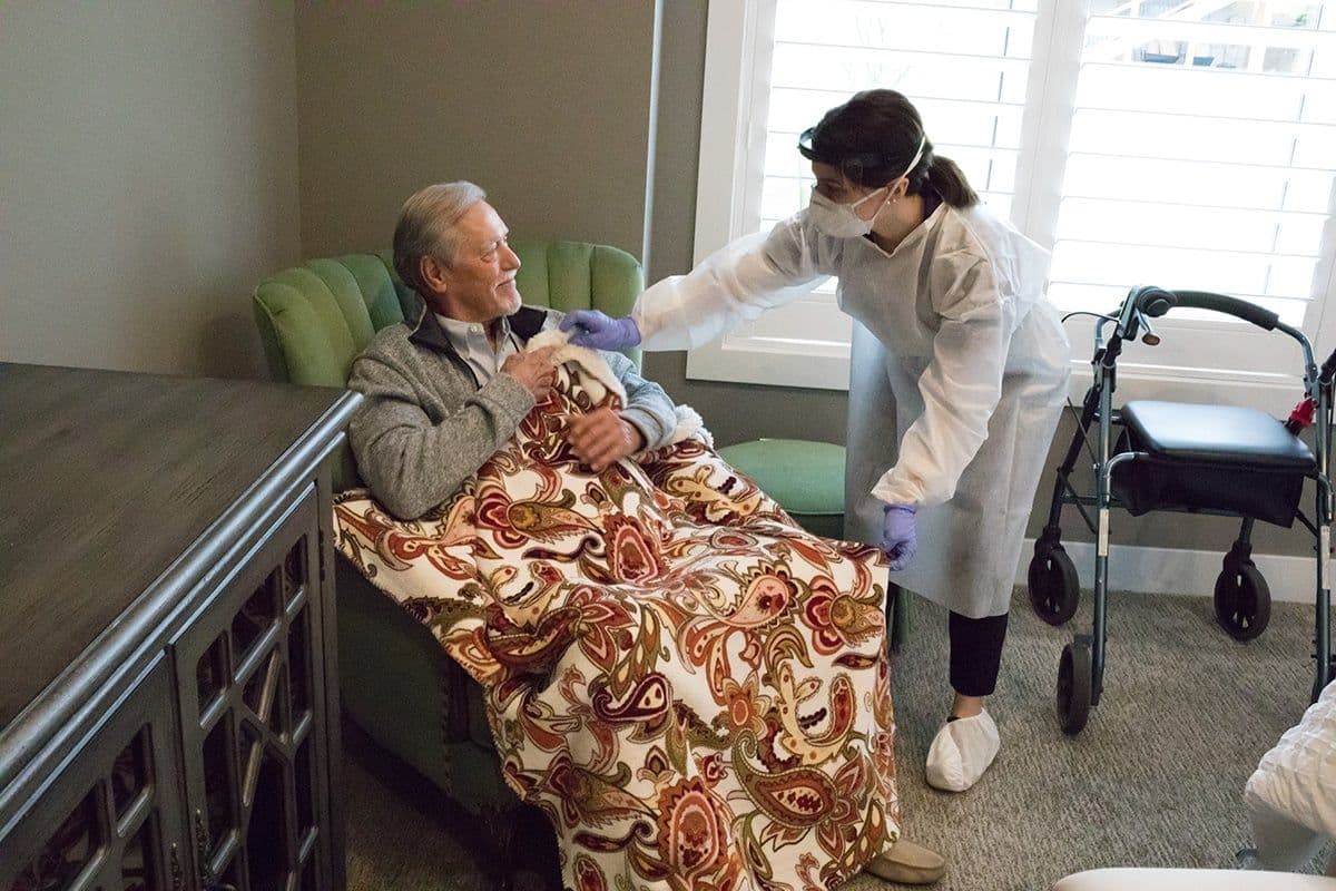 A Home Instead caregiver and an elderly man walk arm-in-arm through a doorway, both smiling, symbolizing trust and companionship in daily activities.