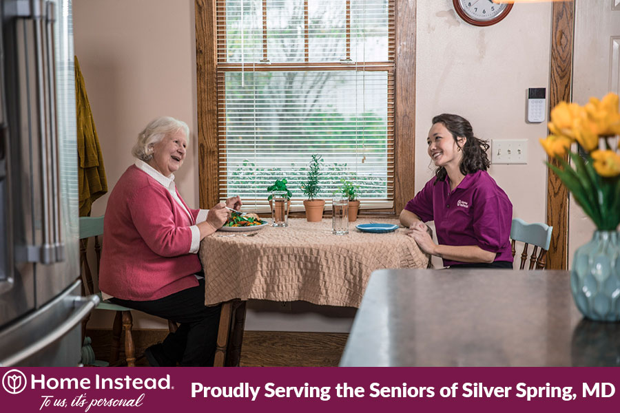Caregiver sitting with an elderly woman at the dinner table eating