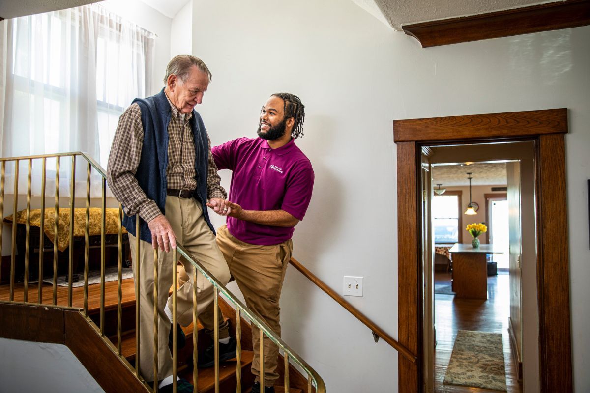 home instead caregiver helping senior man walking down stairs