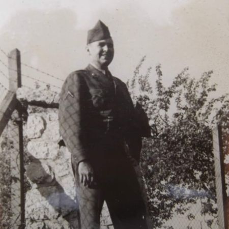 old photo of a soldier standing next to a wire fence