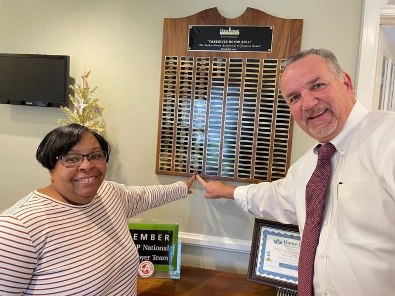 February 2022 Brian Geenty Caring Star Lydia Peterson with owner Brad Snively pointing at the names of past award winners