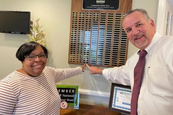 February 2022 Brian Geenty Caring Star Lydia Peterson with owner Brad Snively pointing at the names of past award winners