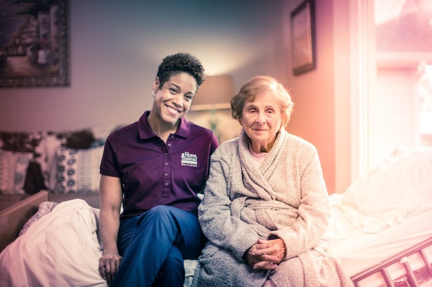 Home Instead Caregiver and aging woman talking and smiling at a table.