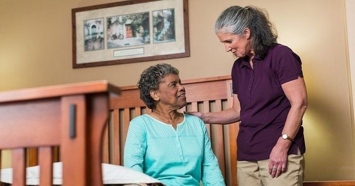 home instead caregiver standing with senior sitting on edge of bed