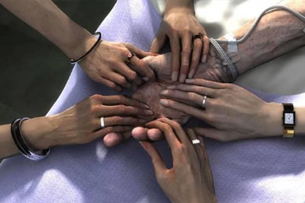 Loving family members holding the hand of an aging adult in a hospital for Palliative Care.