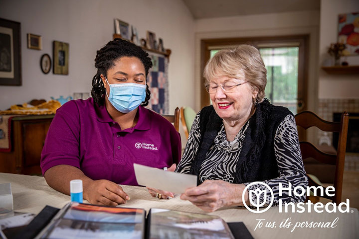 caregiver wearing mask sitting with senior looking at a photo