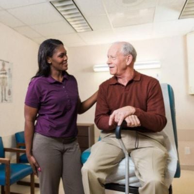smiling caregiver comforting a senior at doctors office