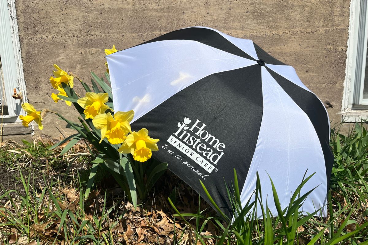 black and white Home Instead umbrella sitting beside some pretty yellow flowers