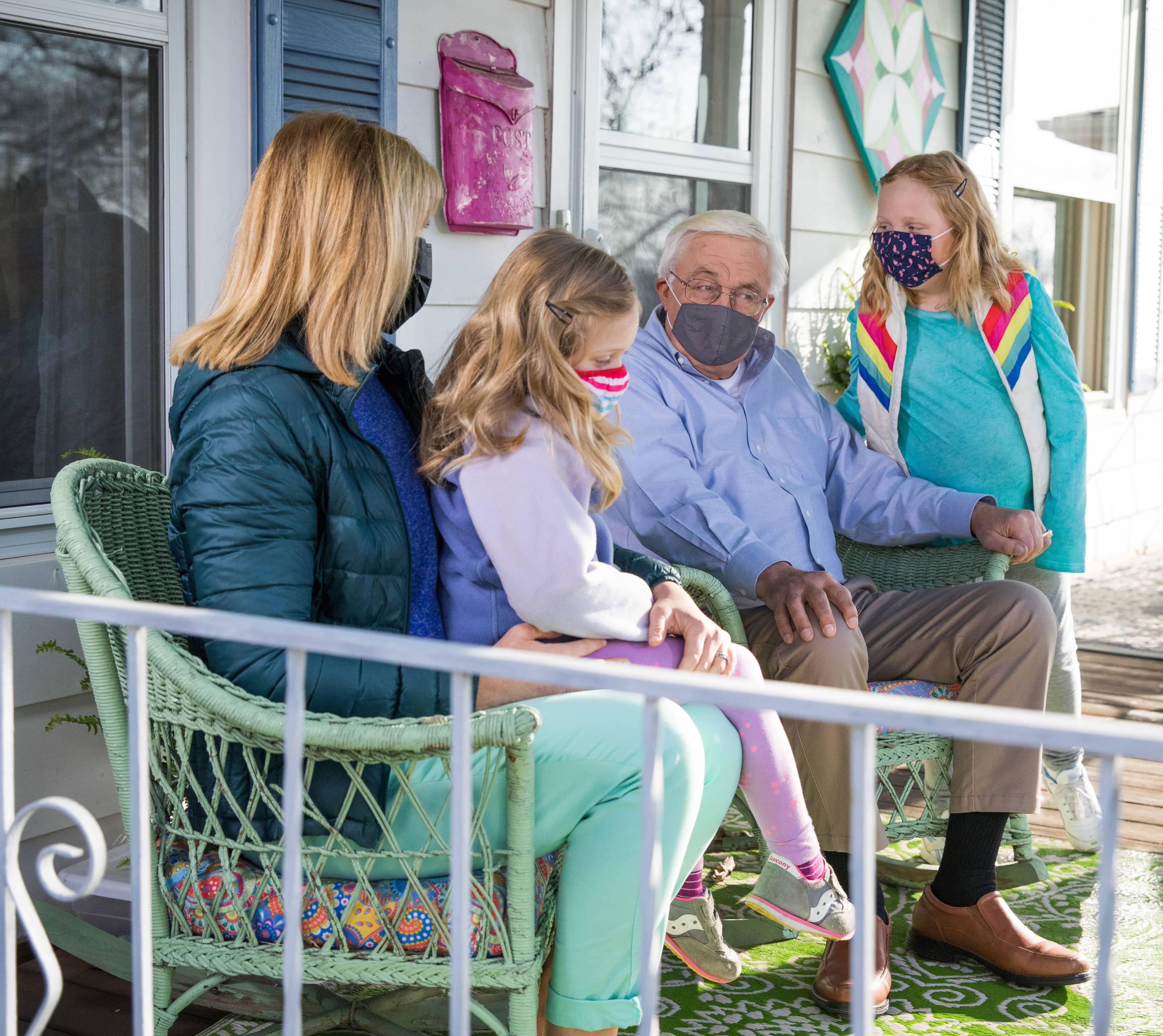 senior sitting with family on front porch wearing PPE