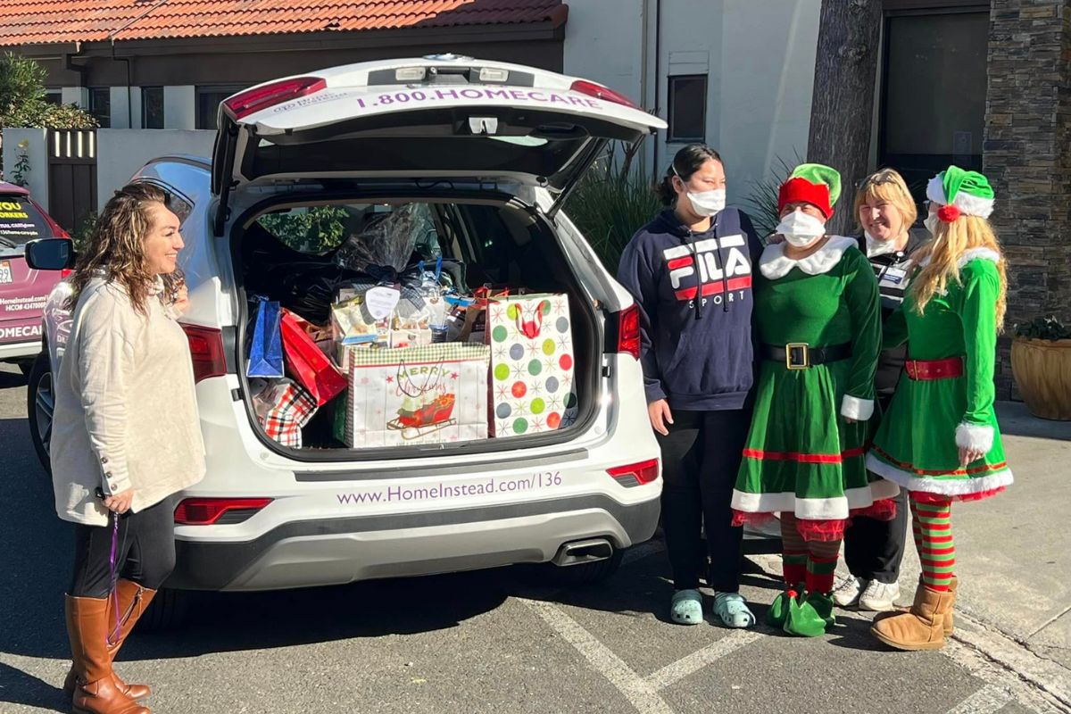 Home Instead employees in elf costumes standing next to Home Instead car full of gifts for seniors