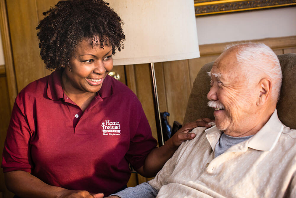 smiling caregiver sitting with a senior in a chair