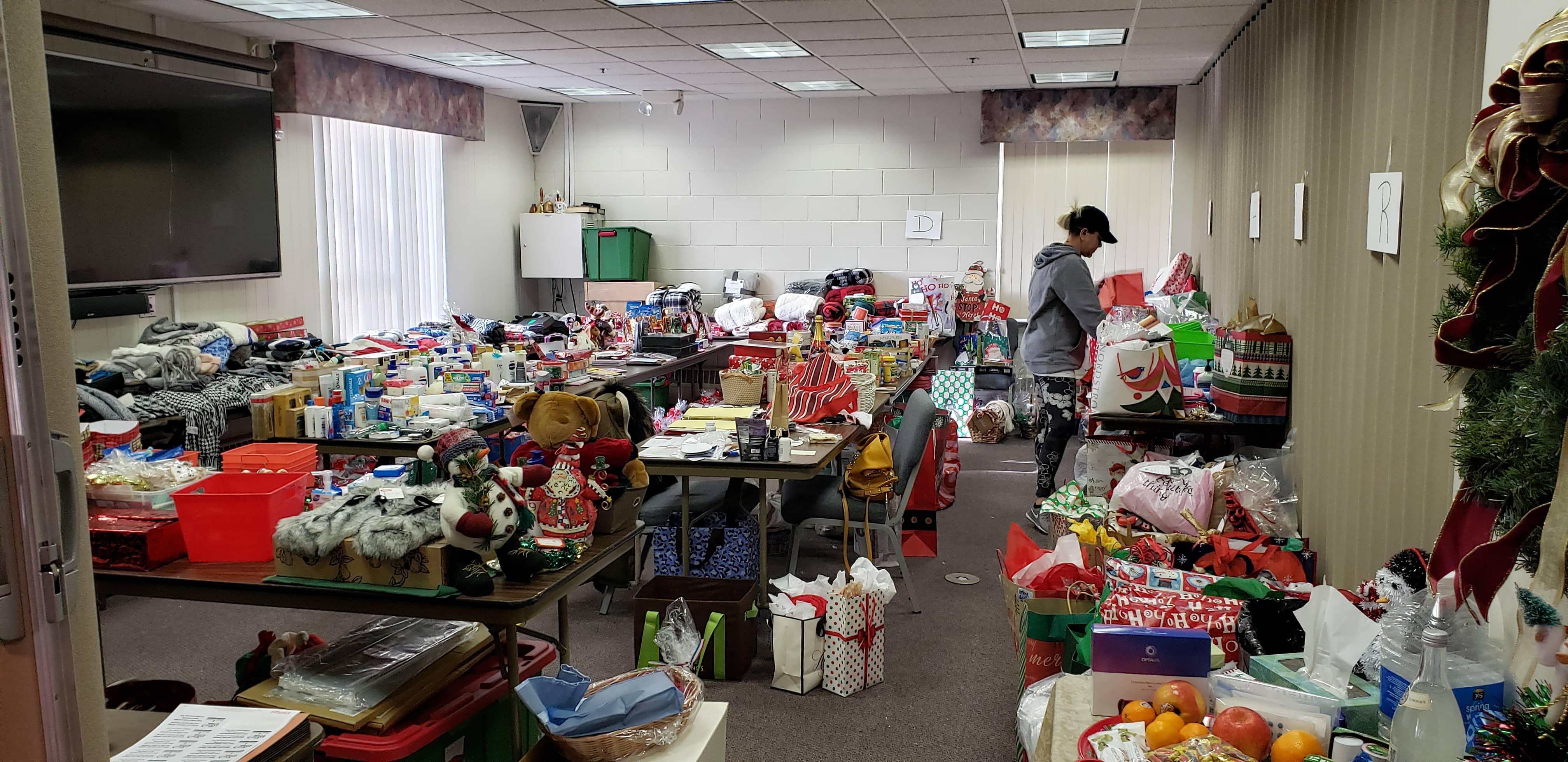 Photo of large conference room with folding table covered in Christmas gift donations and a team member building BASTAS baskets
