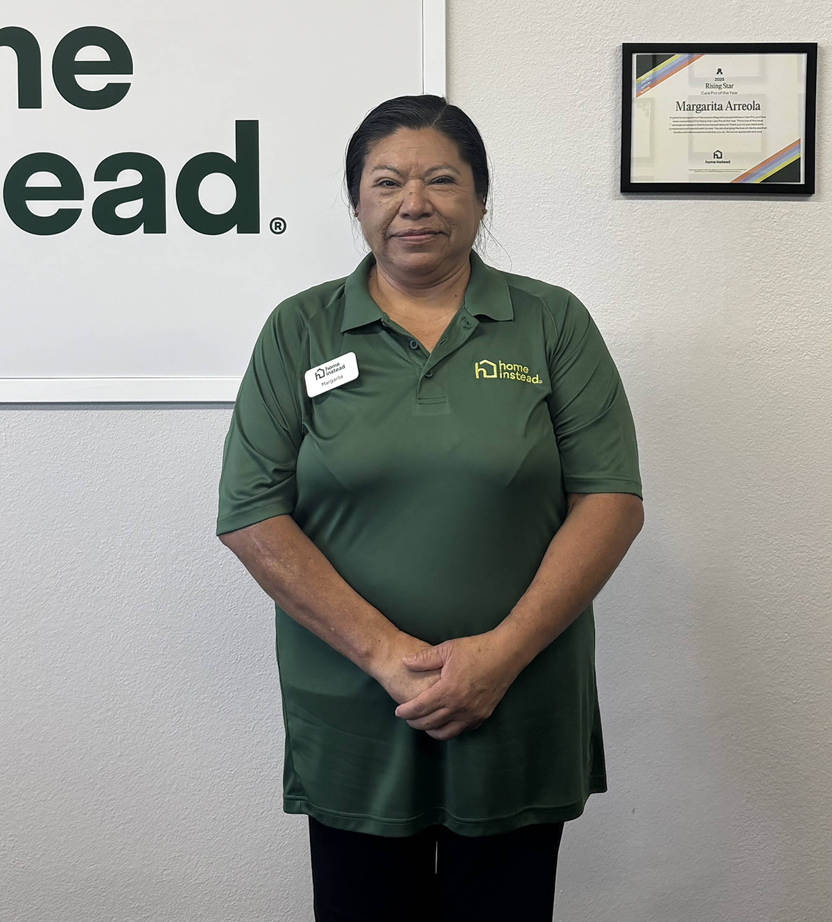 Margarita Arreola standing proudly beside her framed Care Pro of the Year certificate at the Home Instead South Orange County office