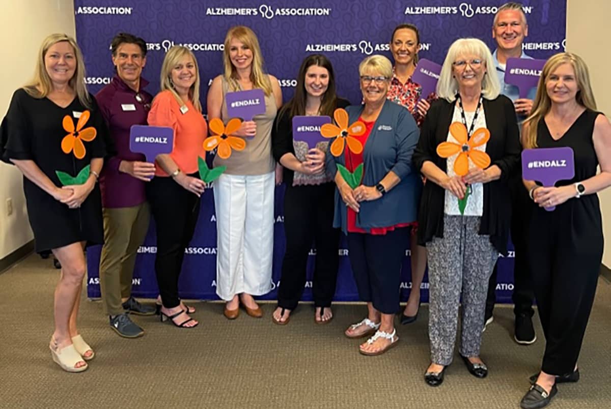 Photo of our team at the Alzheimer's Association Meeting in front of a photo backdrop with the Alzheimer's Association Logo