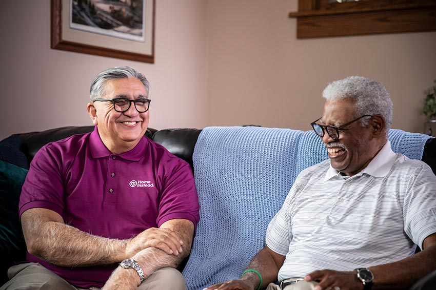 home instead caregiver and senior sitting on couch smiling