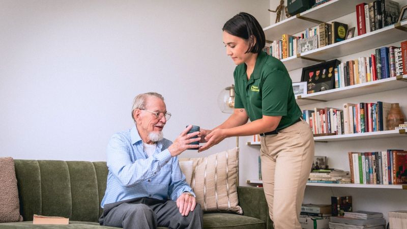 home instead caregiver handing elderly man a cup of tea as part of their companionship care routine