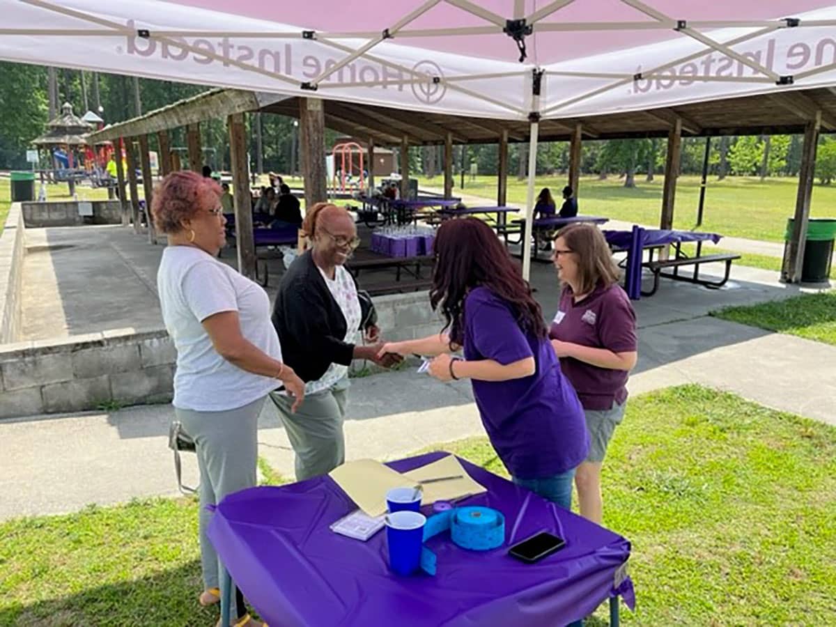 Photo of 4 Home Instead team members at the raffle table for the Home Instead Care Pro Appreciation Picnic. In the background, there is a park and a covered picnic table area.