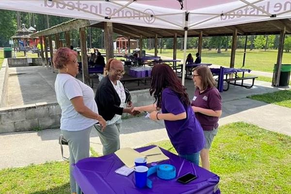 Photo of 4 Home Instead team members at the raffle table for the Home Instead Care Pro Appreciation Picnic. In the background, there is a park and a covered picnic table area.
