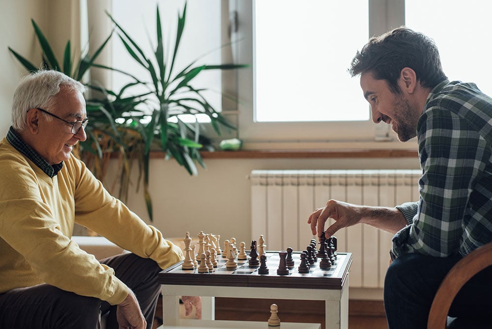happy senior man and caregiver playing chess inside