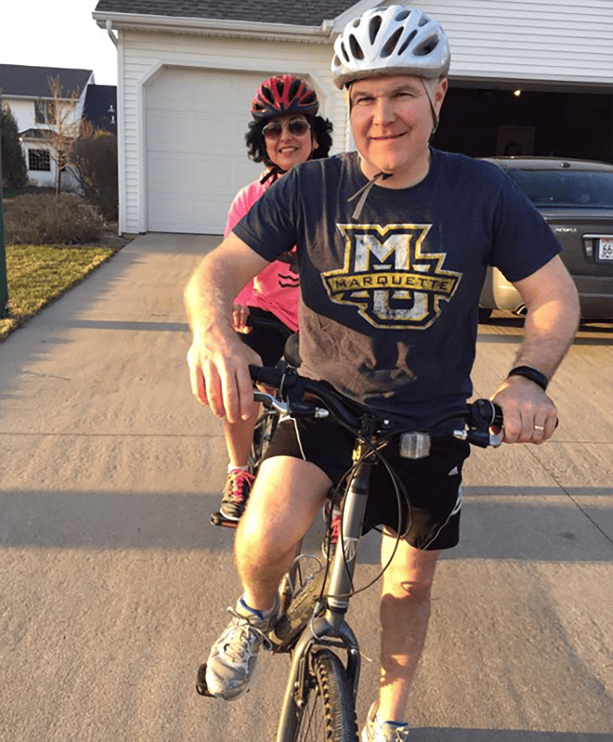Husband & wife on a tandem bike in front of their garage