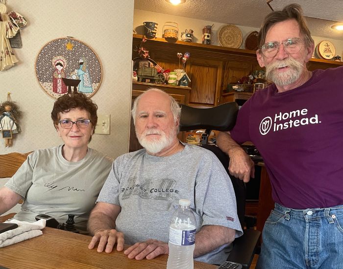 home instead of kansas city missouri caregiver smiling next to two seniors sitting at a table