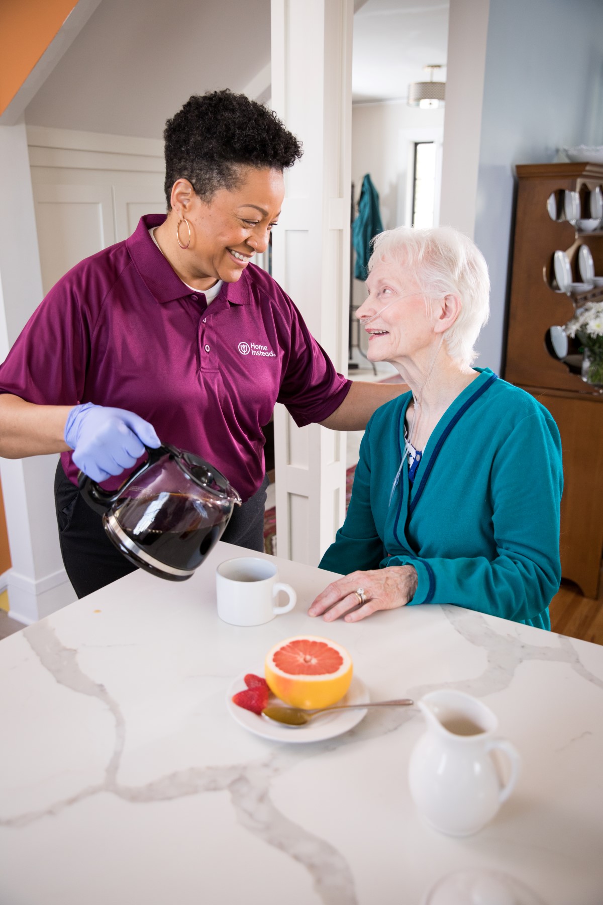 Female caregiver pouring coffee to a senior woman and both are smiling.