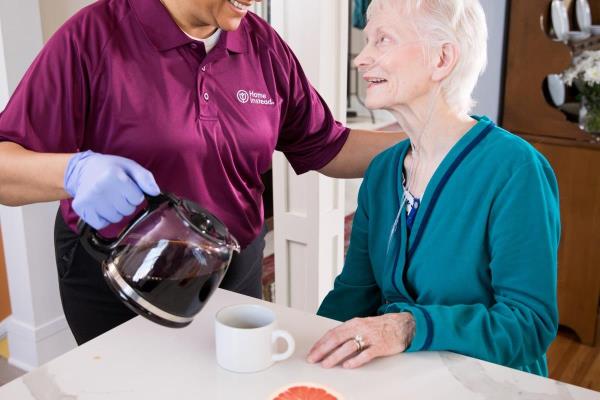 Female caregiver pouring coffee to a senior woman and both are smiling.