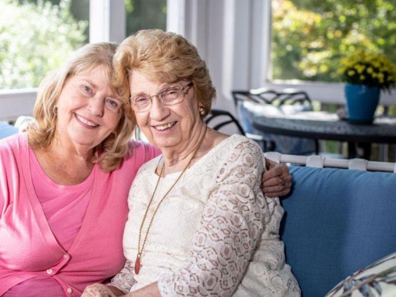 caregiver and client sitting on couch sharing a hug and warm smiles 