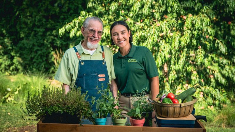 A Home Instead caregiver with an elderly man outdoors, both smiling warmly, showcasing trust and companionship.
