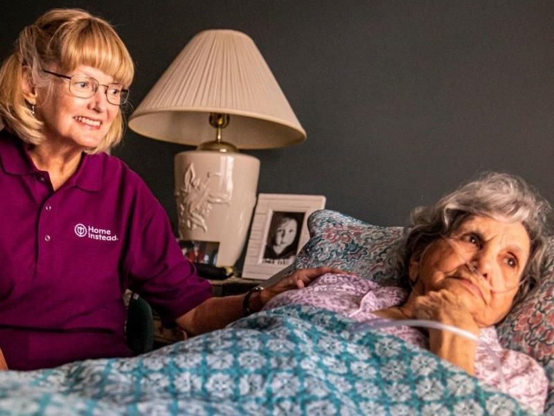 smiling caregiver sitting with senior in bed