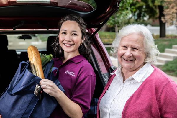 Caregiver anmd edlerly woman unloading groceries from car while smiling