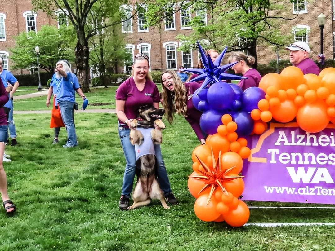 Photo of Home Instead Team Members by the Foothills Alzheimer's Tennessee Walk sign posed with a german shepherd on its back legs