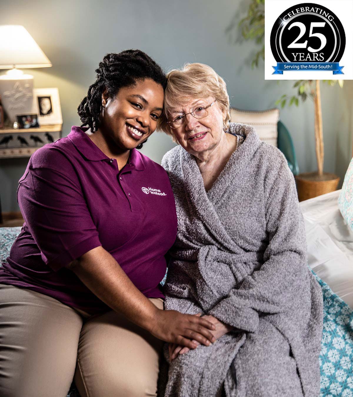 Home Instead CAREGiver and senior sitting on bed smiling with 25 year logo