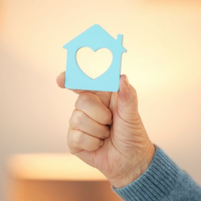 a hand holding a small house figurine that has a heart shape in it