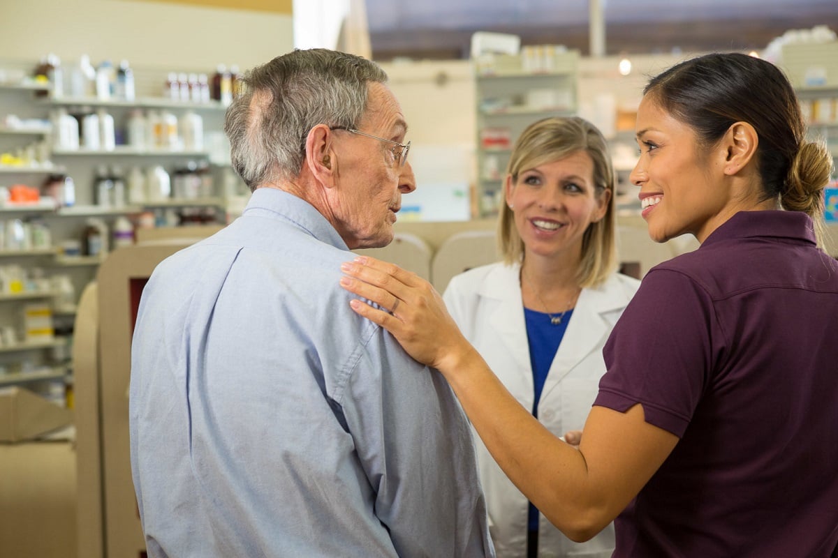 A senior man talks with a caregiver and pharmacist 