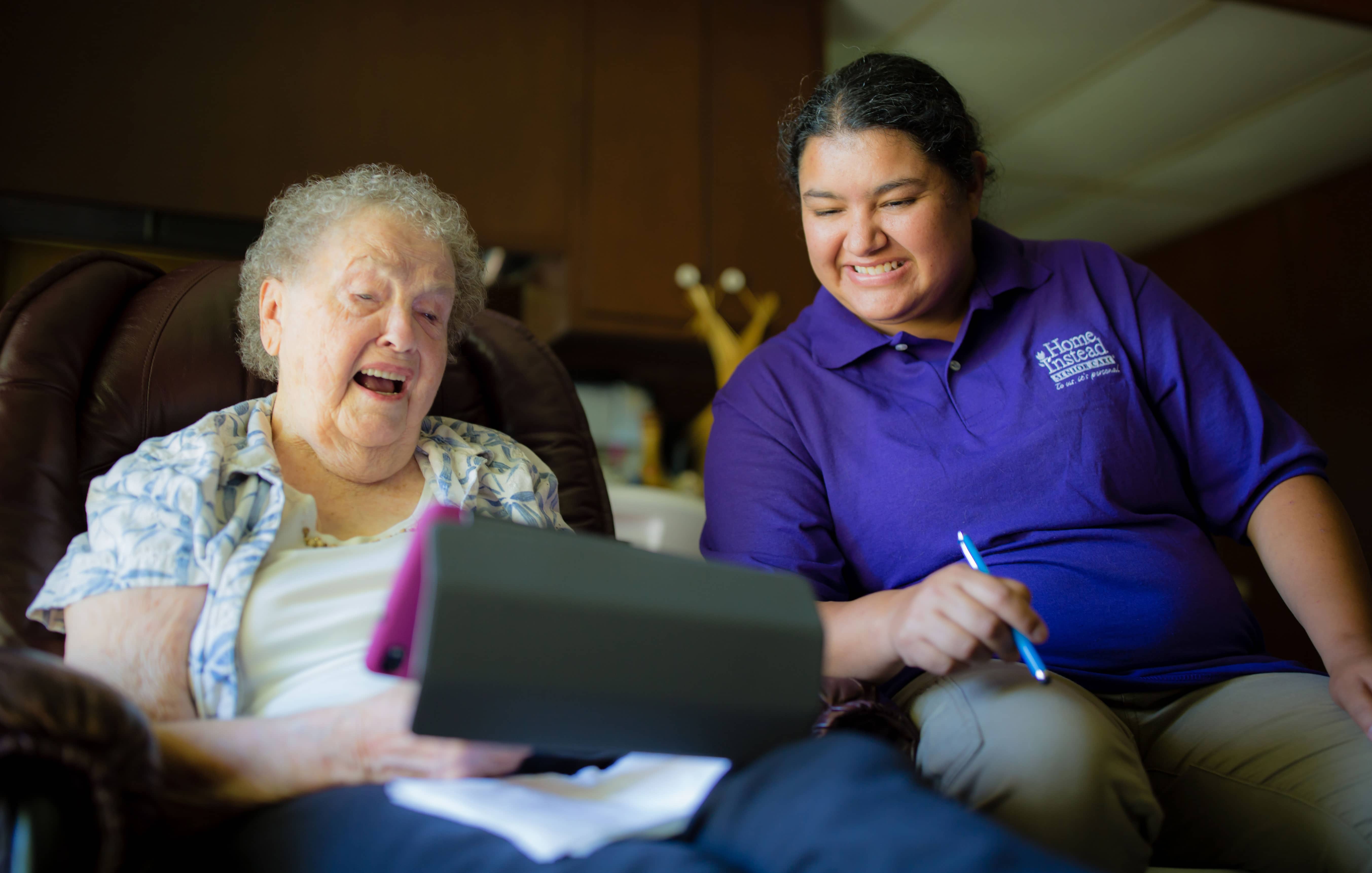 In-Home Caregiver and senior woman sitting and smiling while looking a a tablet
