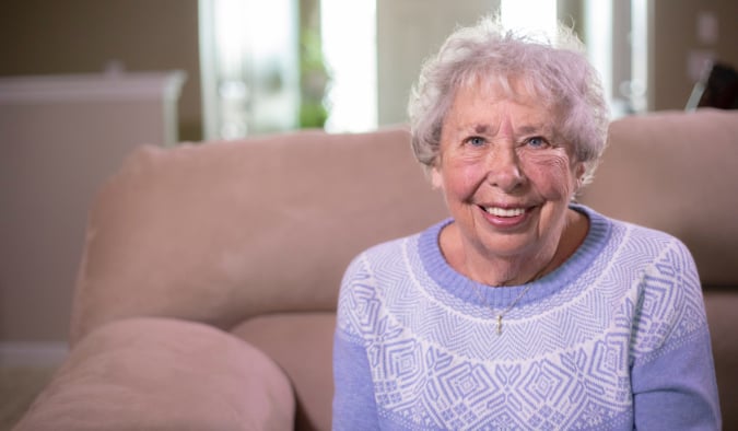 Senior woman with Alzheimer's sitting on sofa and smiling.