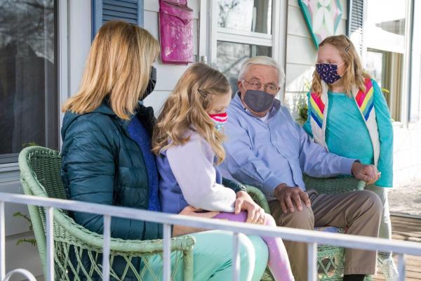 senior man sitting on the porch with his family wearing PPE