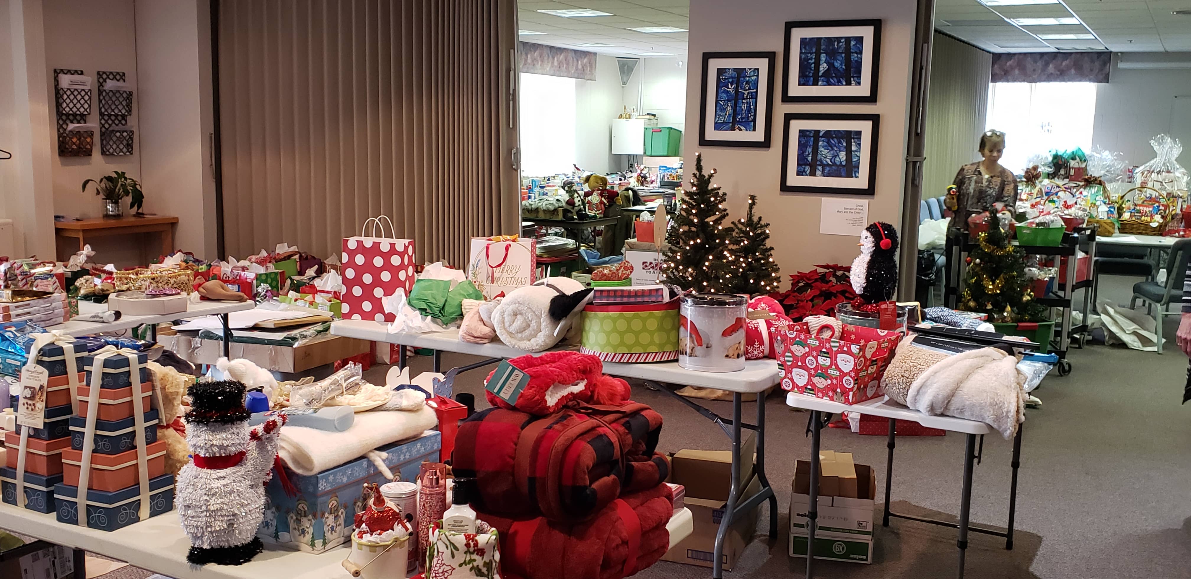 Photo of large meeting room with folding tables that are covered with baskets, blankets and other Christmas gifts