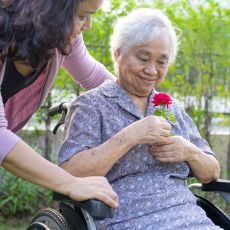 senior holding a rose while a home instead caregiver looks on
